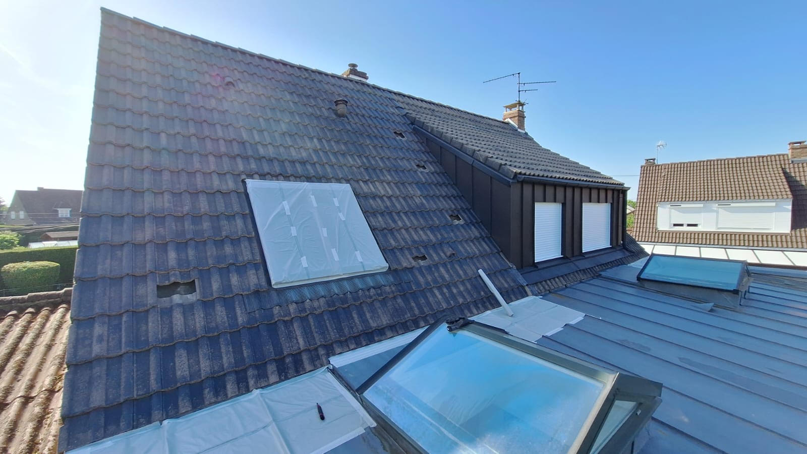 Toiture en tuiles béton vue depuis le toit avant intervention : teinte délavée et irrégulière, surface mate, velux et lucarnes visibles